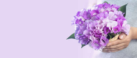 hand holding a basket of fresh purple flowers isolated on a pastel pink background with free space...