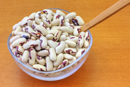 Colorful haricot beans in glass bowl on wooden background