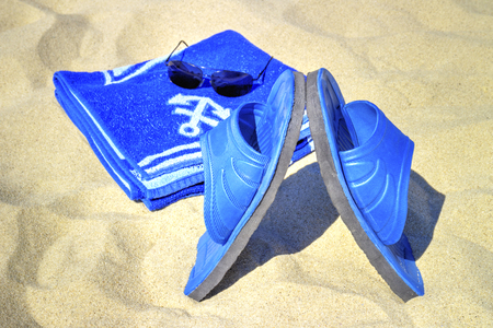 Sunglasses, blue towel and slippers on sandy beachの写真素材