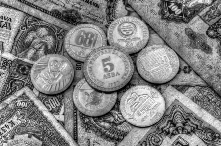 A pile of anniversary coins of republic of Bulgaria over a background of banknotes in black and whiteの写真素材