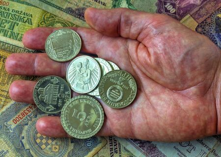 A pile of anniversary coins of republic of Bulgaria in a human's hand over a background of banknotes close up viewの写真素材