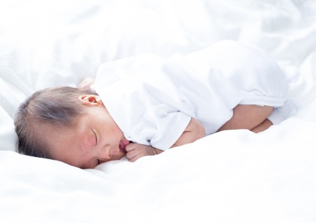 Asian infant baby lying on white bed backgroundの写真素材