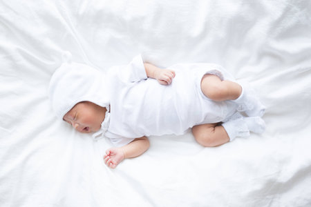 Asian infant baby lying on white bed backgroundの写真素材