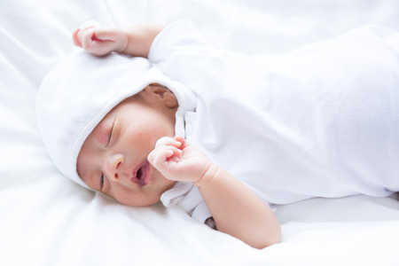 Asian infant baby lying on white bed backgroundの写真素材