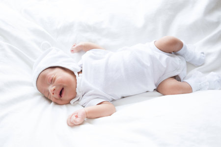 Smiling asian infant baby lying on white bed backgroundの写真素材