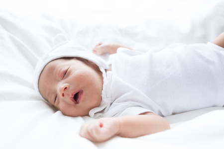 Asian infant baby lying on white bed backgroundの写真素材