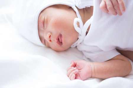 Asian infant baby lying on white bed backgroundの写真素材