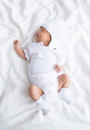 Asian infant baby lying on white bed backgroundの写真素材