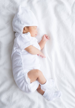 Asian infant baby lying on white bed backgroundの写真素材