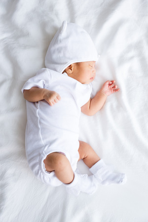 Asian infant baby lying on white bed backgroundの写真素材