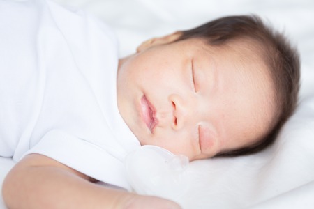 Asian infant baby lying on white bed backgroundの写真素材