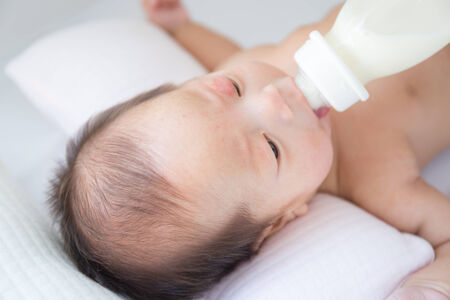 Naked asian infant baby lying on white bed backgroundの写真素材