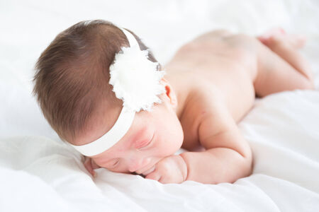 Naked asian infant baby lying on white bed backgroundの写真素材