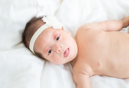 Naked asian infant baby lying on white bed backgroundの写真素材