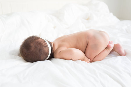 Naked asian infant baby lying on white bed backgroundの写真素材