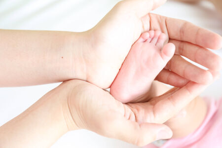 Asian mother playing with her infant baby lying on white bed backgroundの写真素材