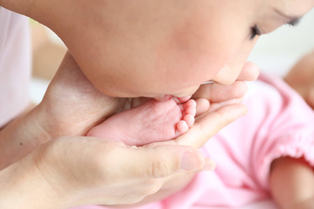 Asian mother playing with her infant baby lying on white bed backgroundの写真素材