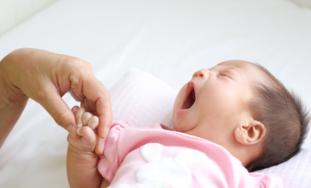 Yawning asian infant baby lying on white bed backgroundの写真素材