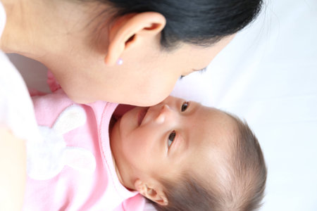 Asian mother playing with her infant baby lying on white bed backgroundの写真素材