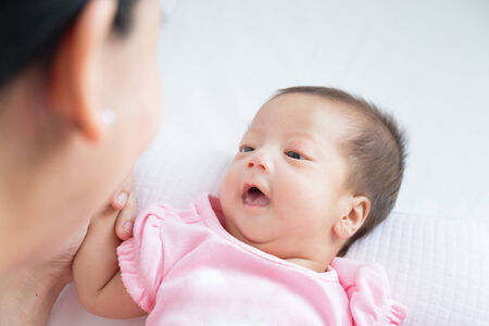 Asian mother playing with her infant baby lying on white bed backgroundの写真素材