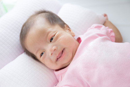 Smiling asian infant baby lying on white bed backgroundの写真素材