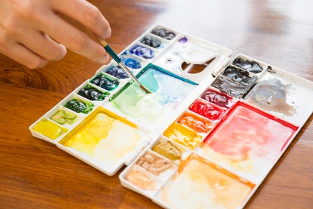 Paintbrush and paint palette with artists hand holding brush painting colorful mixed watercolor