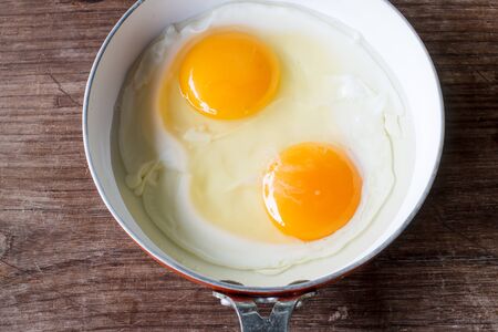 fried eggs sunshine in small pan prepared for breakfast, object put on old wooden backgroundの写真素材