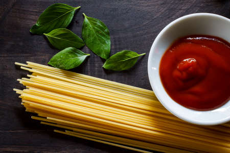 Preparation of spaghetti pasta with tomato ketchup and basil put on black old wooden