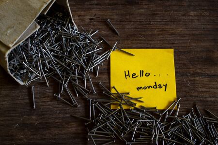 Text "Hello Monday" on yellow short note paper with Iron nails on natural wood desk, still life image dark tone.の写真素材