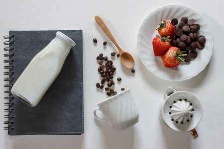 coffee beans,vintage cup, notebook, fresh milk, wood spoon and strawberry with chocolate on white wood background.の写真素材