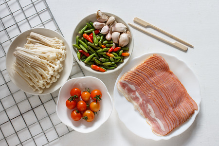 Top view of various ingredients(raw bacon, tomates, Enoki mushroom, chili and garlic put in a small plate) prepareration for dinner party.の写真素材