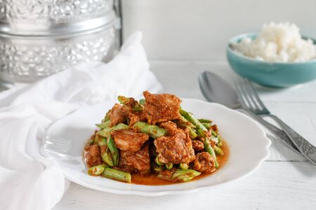 Authentic local Thai food: Red curry pork with yard long bean serve with steamed jasmine rice put on white wood table.の写真素材