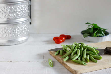 Chopped Yard long bean on cutting board with cherry tomatoes and Thai basil prepare for cook.