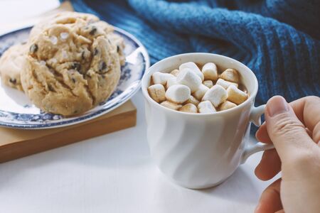 hot chocolate with marshmallows in a ceramic cup warm knitted sweater and chocolate chip cookies.の写真素材