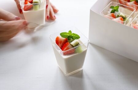 Healthy breakfast with yogurt and mixed fruit in plastic cup in box set. hand in frame.