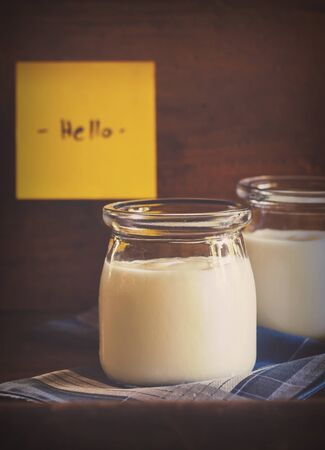 Greek yogurt in a glass jars with text "Hello" on yellow short note paper and wooden background, still life image dark tone.の写真素材