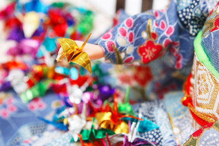 Miniature origami birds and a Japanese doll dressed in kimono. Shallow depth of field. Focus on the golden bird.の写真素材