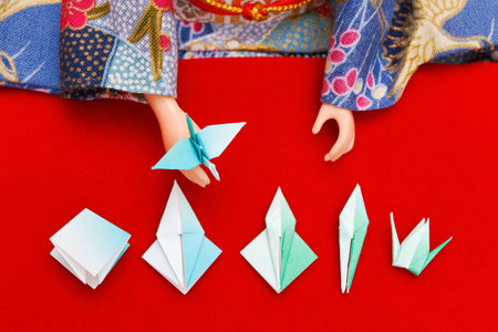A Japanese doll dressed in kimono showing the steps to fold a paper birdの写真素材