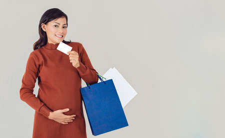 Pregnant Asian woman holding shopping bag and white card   and smiling face.