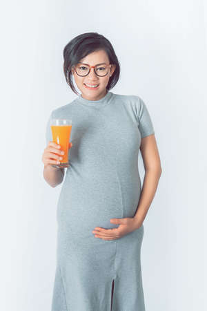 Asian pregnant women  are happy to drink healthy orange juice Stand on a white background. Focus on  faceの写真素材