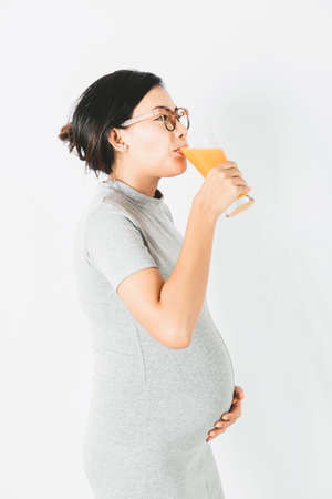 Asian pregnant woman standing drinking orange juice In a relaxed mood.Focus on face