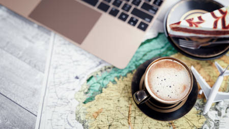 Coffee cups, notebooks, plane cakes and maps are placed on the table.の写真素材