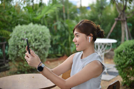 Young woman talking in video chat via digital mobie white wireless .while sitting in her favorite in gardenの写真素材