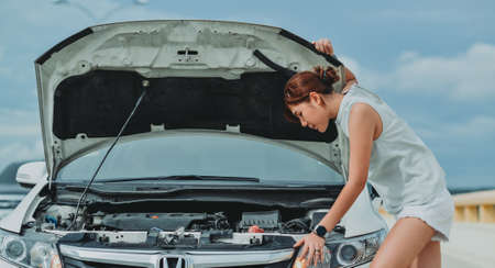 Young woman standing near broken down car with popped up hood having trouble with her vehicle. Female driver waiting for help beside malfunction auto.の写真素材