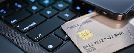Close-up of a credit card placed on a laptop keyboard next to a smartphone displaying financial...