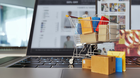 A small shopping cart filled with colorful bags and boxes sits on top of a smartphone and laptop. 3d, rendering, illustration,の写真素材