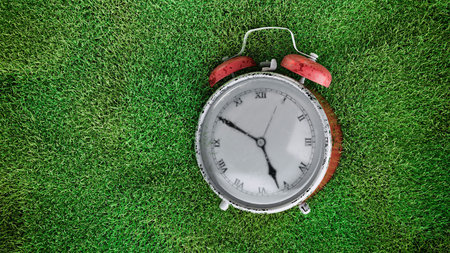 Classic red alarm clock on green grassy surface retro nostalgic concept symbolizing time and memory vintage still lifeの写真素材