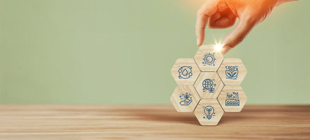 Hand holding connected wooden hexagon blocks with business icons for idea sustainability finance research and teamwork on desk with soft background symbolizing corporate strategy and planningの写真素材
