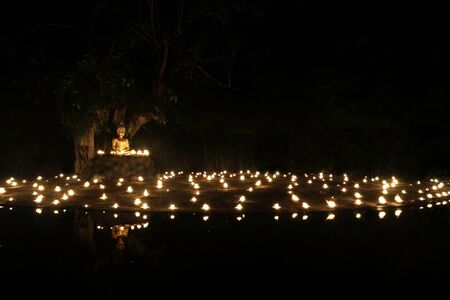 Buddha statue reflect on water with candles fire lighting. (Lord Buddha Day at Phan Tao Temple Chiangmai, Thailand)の写真素材
