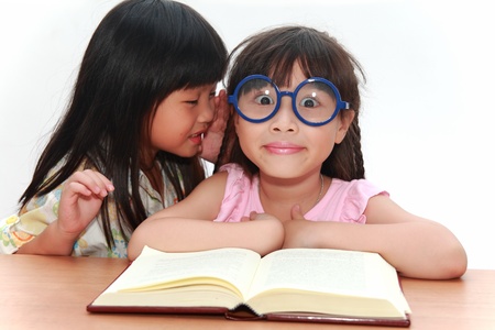Cute little asian girl whispering something to her sisterの写真素材